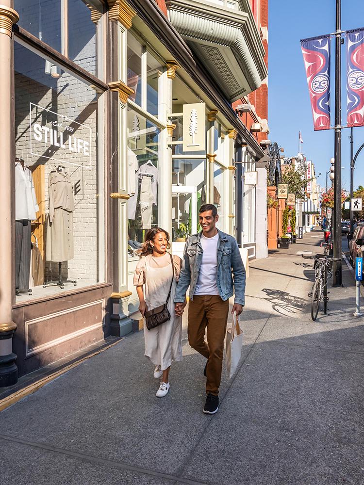 A young couple walks hand-in-hand down Lower Johnson street while shopping in Victoria, BC