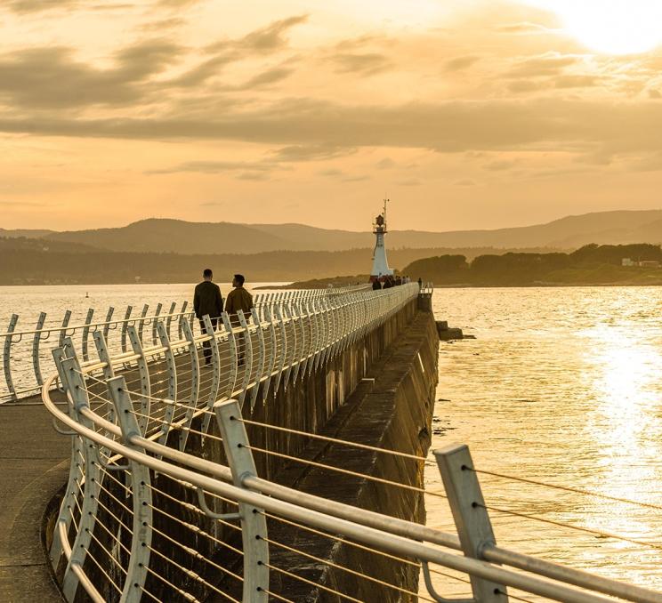 A male couple walks along the Ogden Point Breakwater at sunset in Victoria, BC