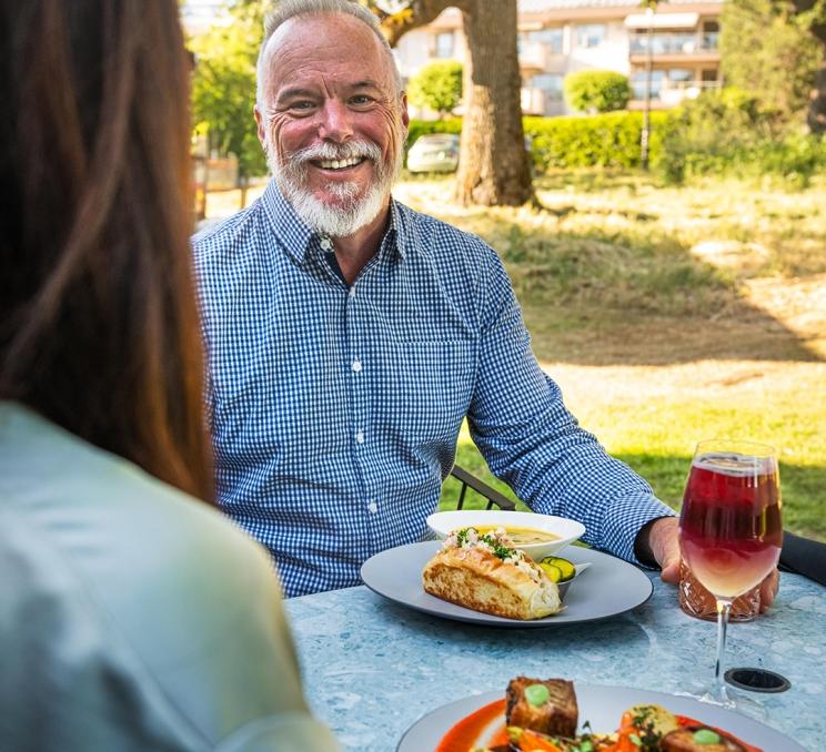 A man in a blue shirt looks towards a woman as they dine on the patio at Fireside Grill in Victoria, BC