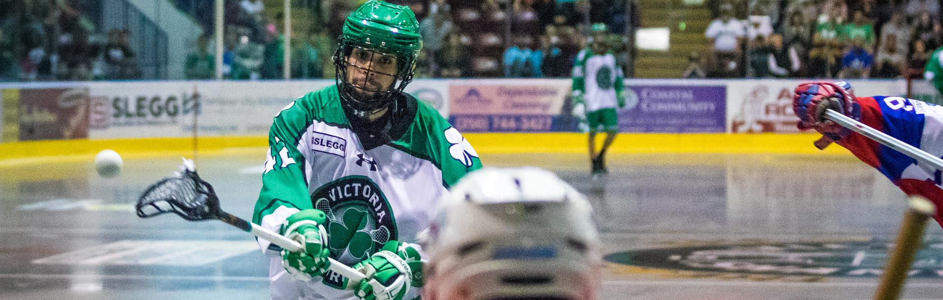 A Victoria Shamrocks player wearing white and green shoots the ball on a goalie during a lacrosse game in Victoria, BC
