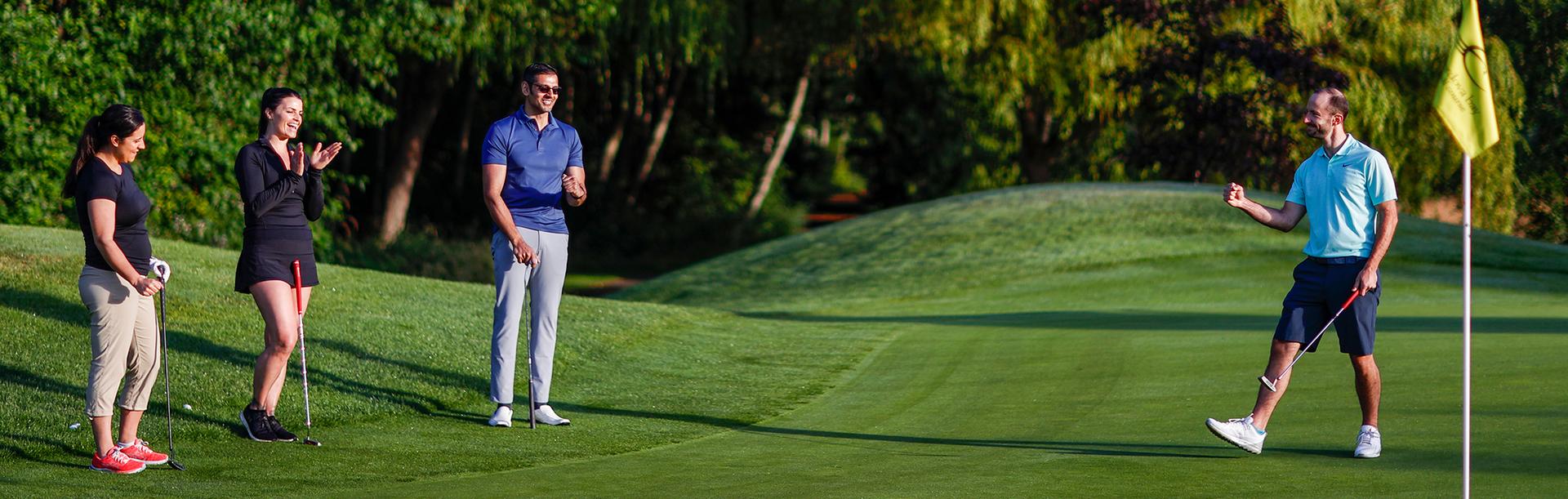 A golfer celebrates sinking a put with his colleagues on a golf course in Victoria, BC
