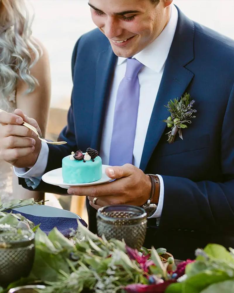 A groom dressed in blue tucks into a blue dessert at a wedding in Victoria, BC