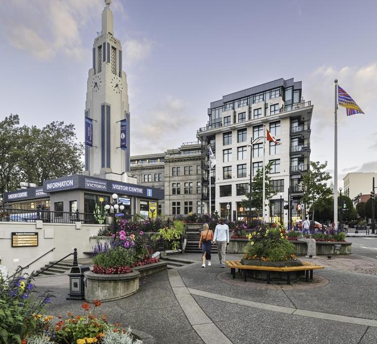 A couple walks hand-in-hand past flowers outside of the Victoria Visitor Centre in downtown Victoria, BC
