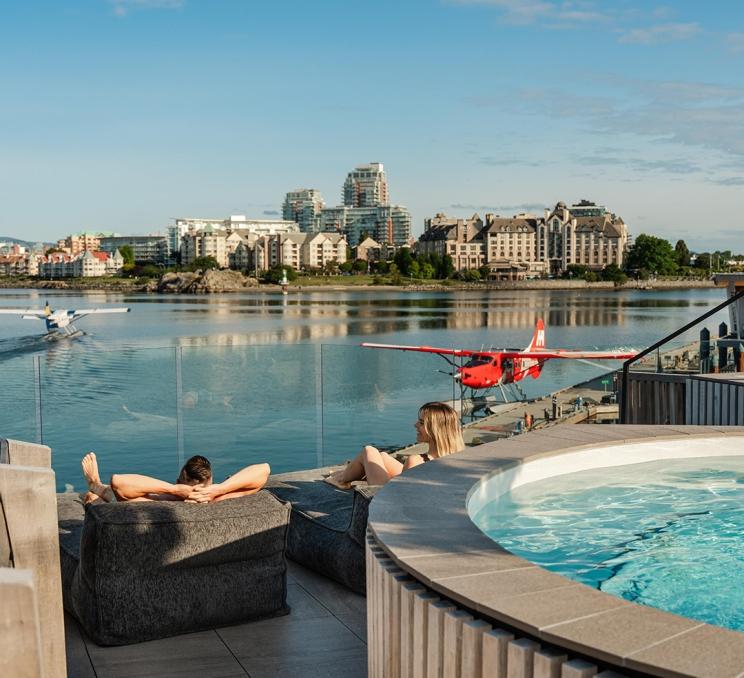 A couple rests on lounge chairs on the deck of HAVN Saunas overlooking the Inner Harbour of Victoria, BC