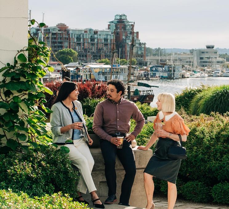 A group of delegates chat in the garden at the Inn at Laurel Point with the Inner Harbour behind them in Victoria, BC