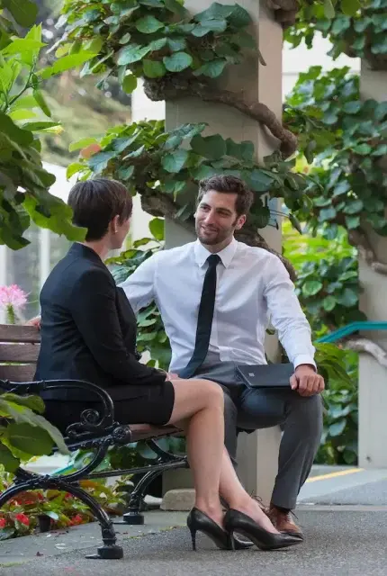 A man and woman sit on a bench, engaged in a lively conversation, enjoying each other's company in a sunny park