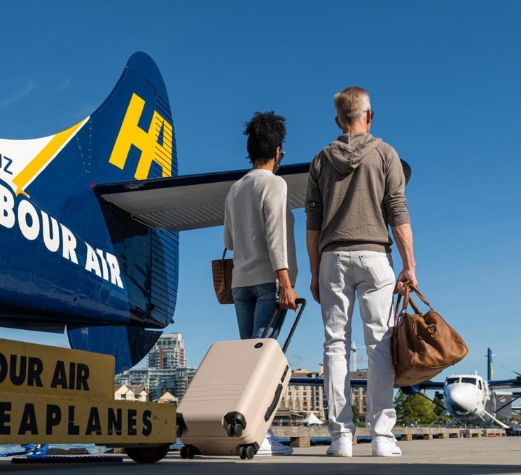 A man and a woman carrying a pink suitcase arrive in Victoria, BC after disembarking a Harbour Air Seaplane flight in the Inner Harbour