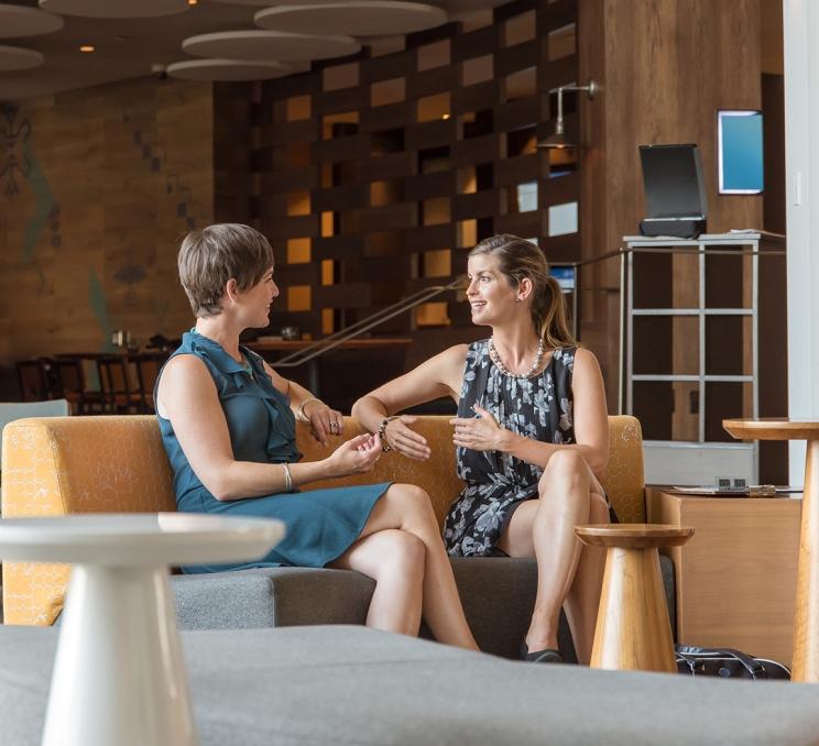 Two women in dresses have a conversation in the lobby of the Delta Hotels by Marriott Victoria Ocean Pointe Resort in Victoria, BC