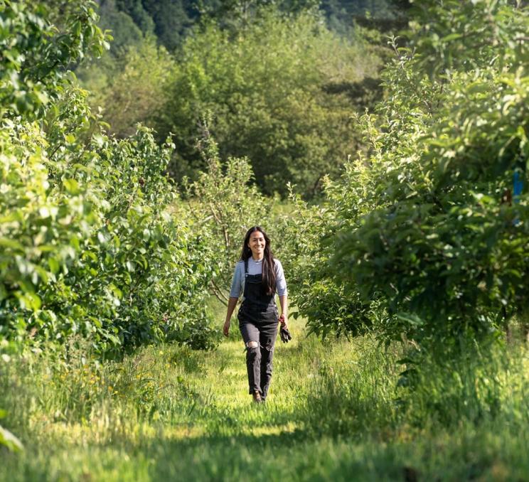 A young female farmer, dressed in black overalls, walks through an orchard during spring at 10 Acres Farm on the Saanich Peninsula in Greater Victoria, BC