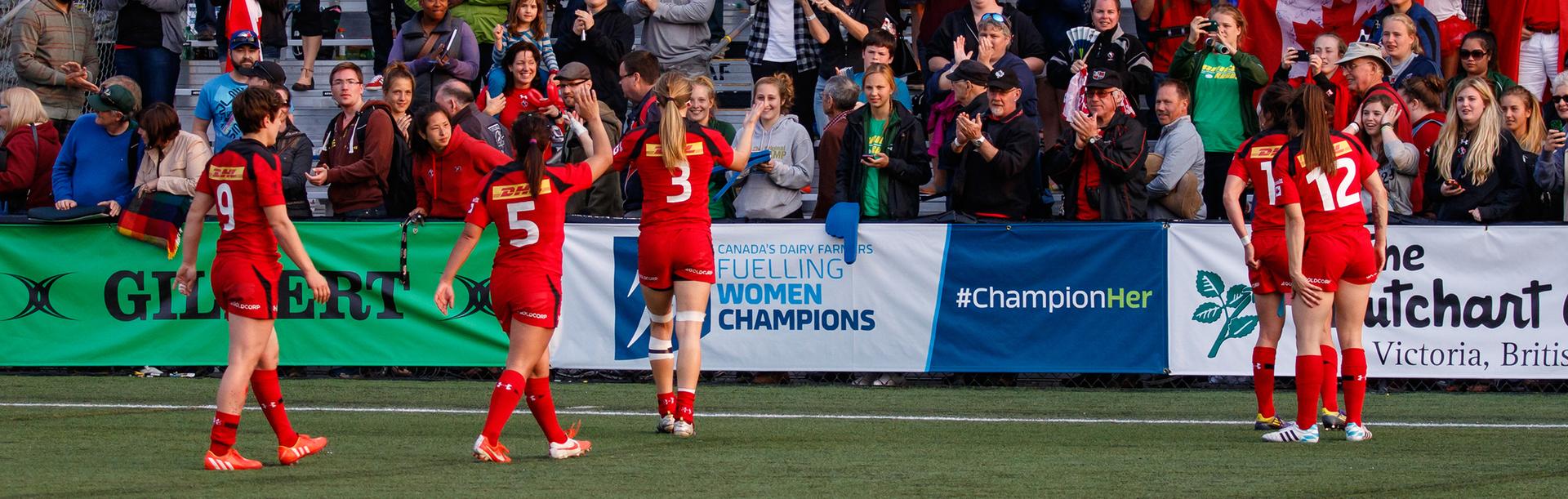 A group of Women's Rugby Sevens players wearing red celebrate with the crowd after a win at Starlite Stadium in Greater Victoria, BC