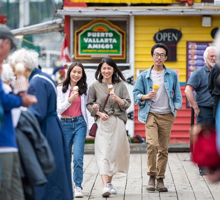 A family walks in front of a yellow building along the dock at Fisherman's Wharf in Victoria, BC