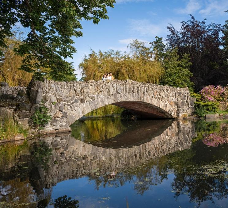 A family stands atop a stone bride over a pond in Beacon Hill Park in Victoria, BC