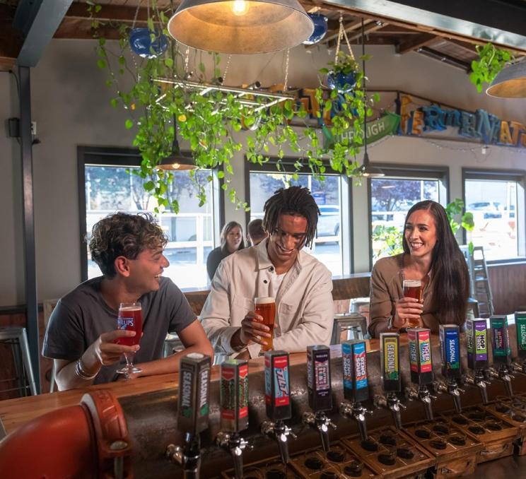 Three friends enjoy beers at the bar at Phillips Brewing and Malting Company's tasting room in Victoria, BC