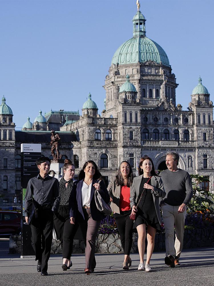 A group of professionals walk in front of the BC Parliament Buildings in Victoria, BC