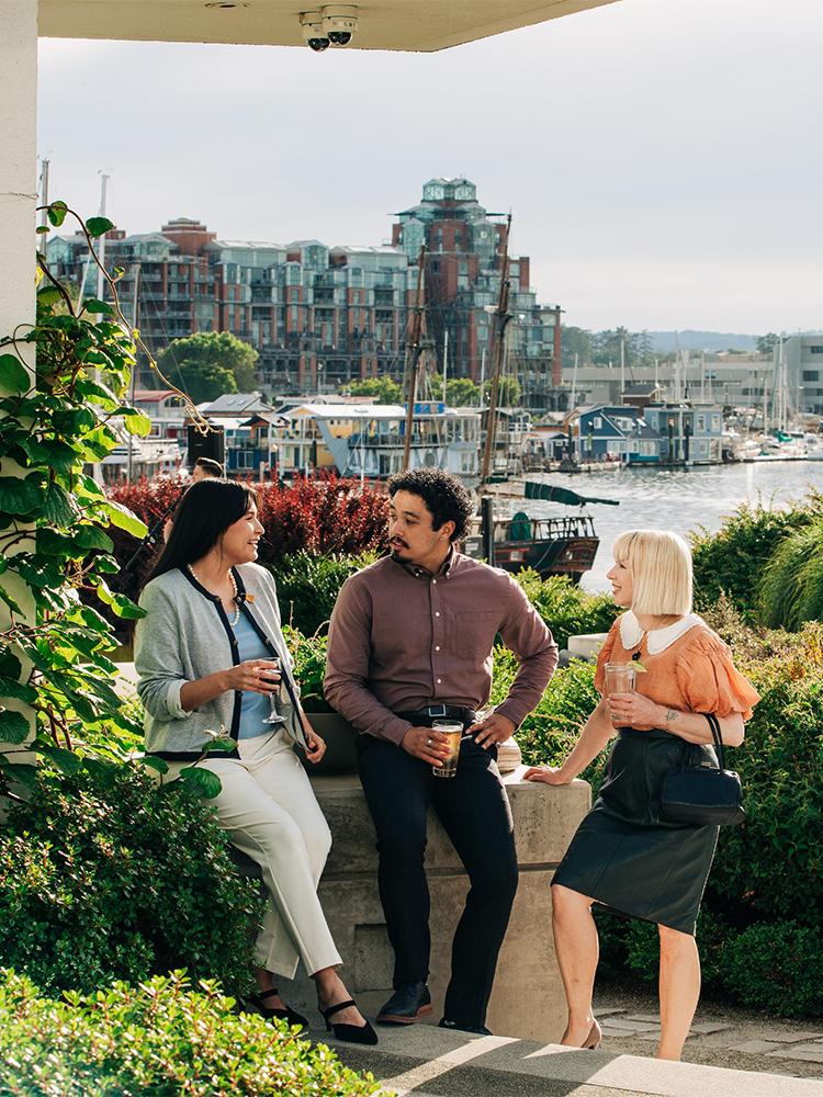 A group of professionals have a conversation in the garden at the Inn at Laurel Point, with Fisherman's Wharf in the background, in Victoria, BC