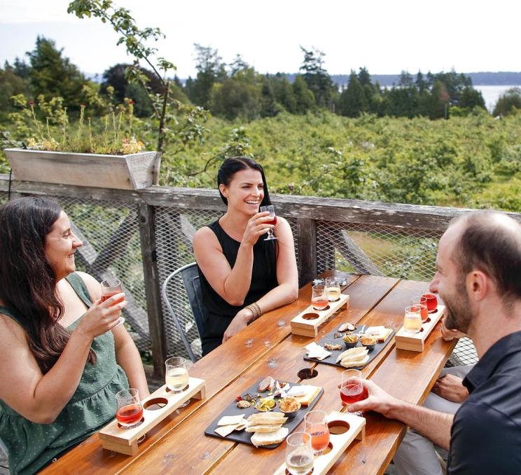 A group of friends enjoy cider flights and charcuterie boards while on the patio at Sea Cider Farm & Ciderhouse in Victoria, BC