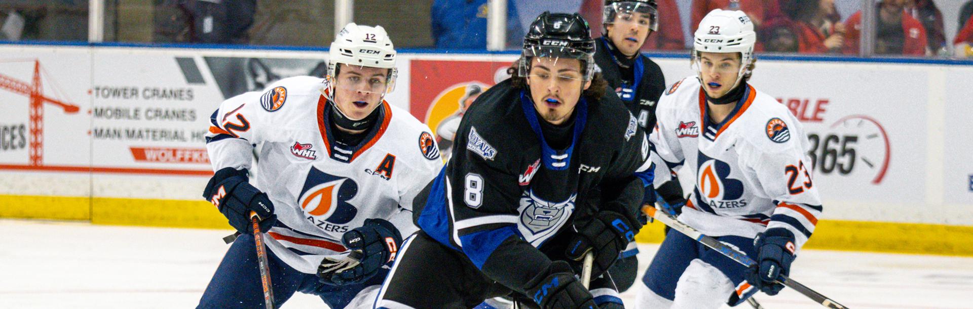 A Victoria Royals player in a blue on black jersey passes two Kamloops Blazers players during a WHL hockey game in Victoria, BC