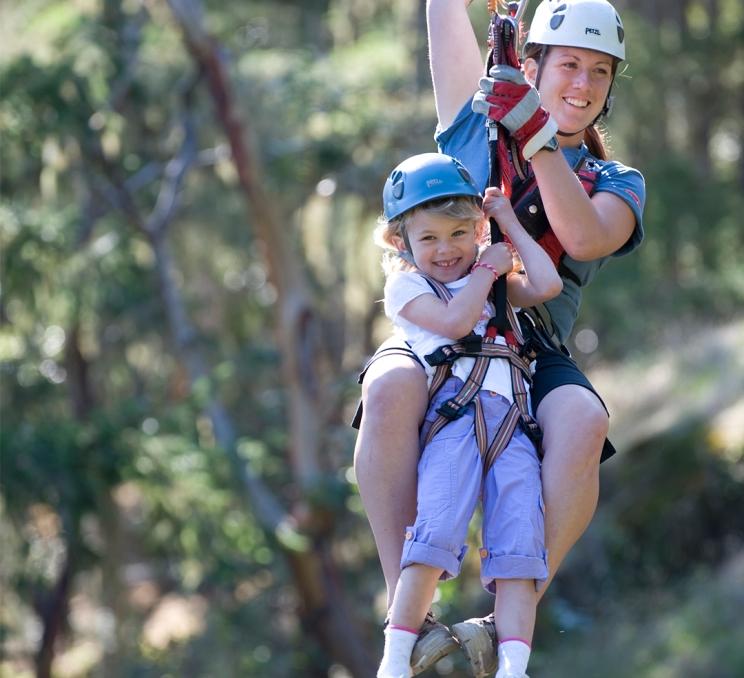 A mother and daughter zip along a zipline through the trees at Adrena Line Zipline Adventures in Victoria, BC